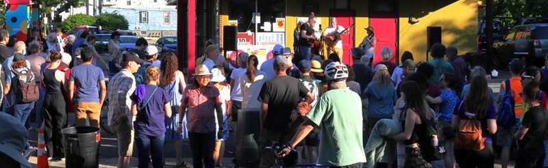 Large, festive crowd listening to band at vibrantly painted gas station